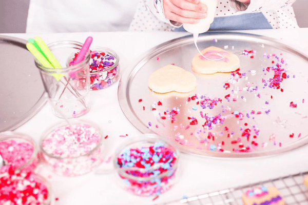 Heart shaped cookies on tray being decorated with pink sparkles